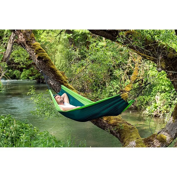 Amazonas Hängematte Silk Traveller forest - L x B: 220 x 140 cm, Grün - Entspannung pur: Ein Mann genießt die Ruhe in einer grünen Hängematte, befestigt an moosbewachsenen Ästen über einem friedlichen Fluss.