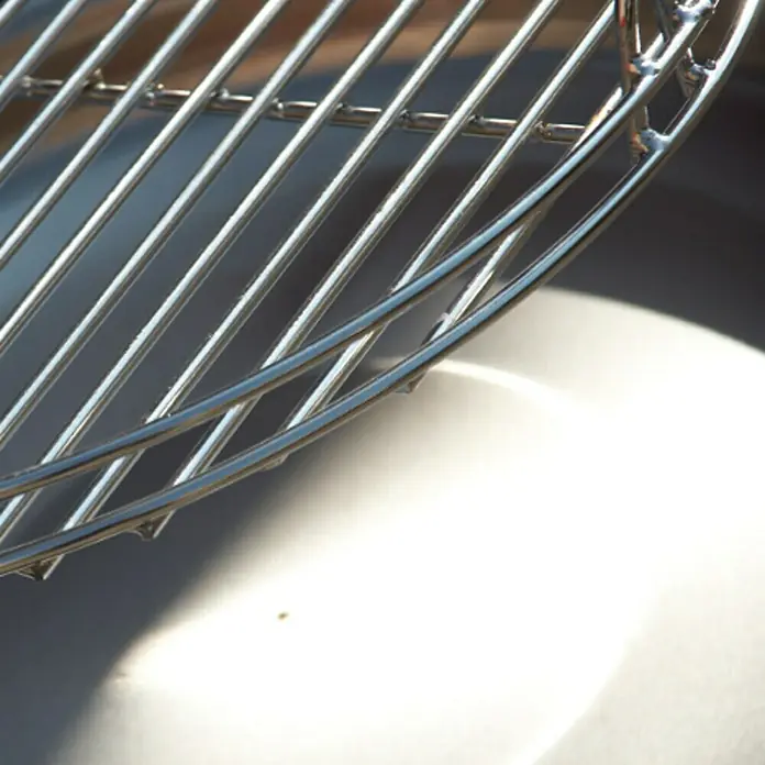 Grillrost - Durchmesser: 50 cm - Nahaufnahme eines glänzenden Grillrosts, der die Metallstruktur und das reflektierende Licht betont.\n