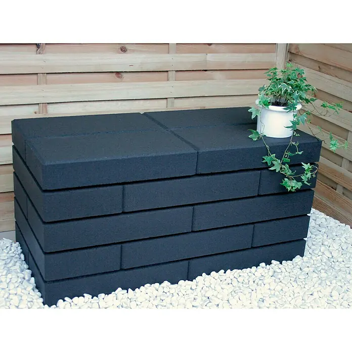 Christoph Mauerstein C-Line - Anthrazit, 50 x 25 x 10 cm, Beton - Das Bild zeigt eine stilvolle, schwarze Steinbank im Freien, die mit einem Topf mit Efeu dekoriert ist. Die Bank steht auf weißen Kieselsteinen.