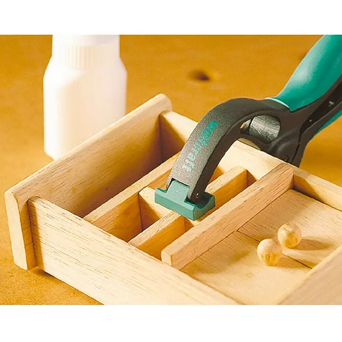 Wolfcraft Federzwinge FZ 40 - Spannweite: 40 mm, Ausladung: 40 mm - Nahaufnahme einer Werkbank mit einer Holzkiste, einer Flasche Kleber und einer Wolfcraft Einhandzwinge zum Fixieren der Holzteile.