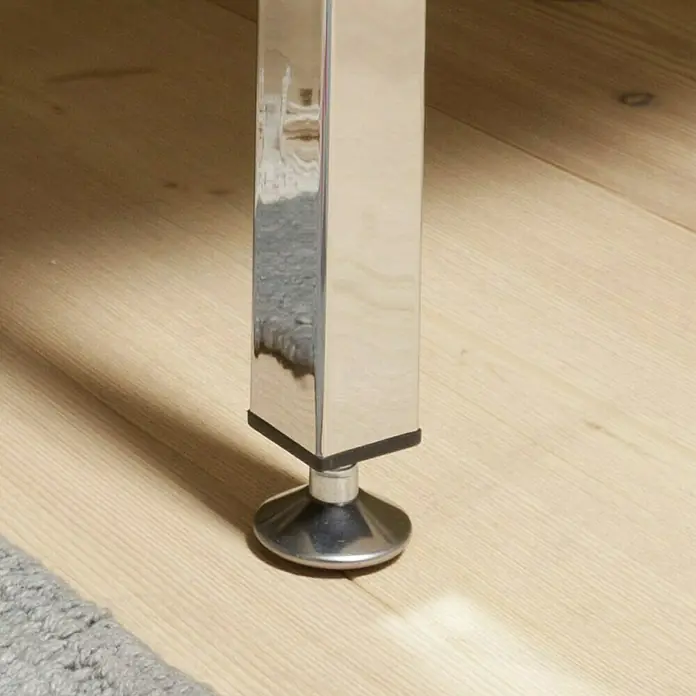 Element System Möbelfuß - 2,5 x 2,5 x 20 cm, Traglast: 30 kg, Stahl, Chrom - Nahaufnahme eines verchromten Möbelbeins mit rundem Fuß auf einem hellen Holzboden, das die moderne Ästhetik und die Details des Designs hervorhebt.