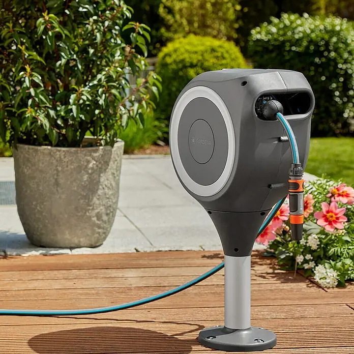 Gardena Schlauchbox Roll-Up S - Schlauchlänge: 15 m, 360 ° drehbar - Der Gardena Schlauchbox RollUp M/L auf einem Holzdeck, umgeben von Pflanzen, bietet bequeme Gartenbewässerung mit automatischer Aufrollfunktion.