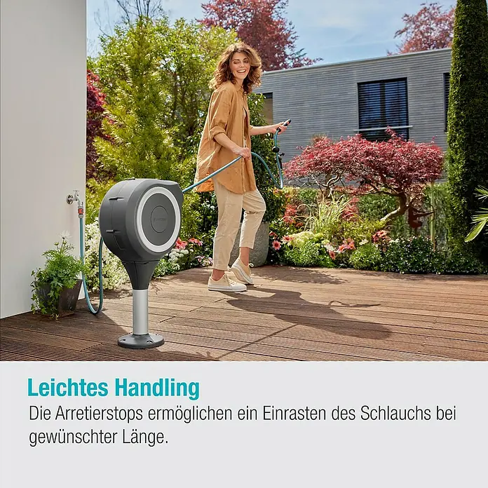 Gardena Schlauchbox Roll-Up S - Schlauchlänge: 15 m, 360 ° drehbar - Eine Frau benutzt eine Gardena Schlauchbox auf einer Holzterrasse. Die Schlauchbox ist grau mit einem silbernen Standfuß.