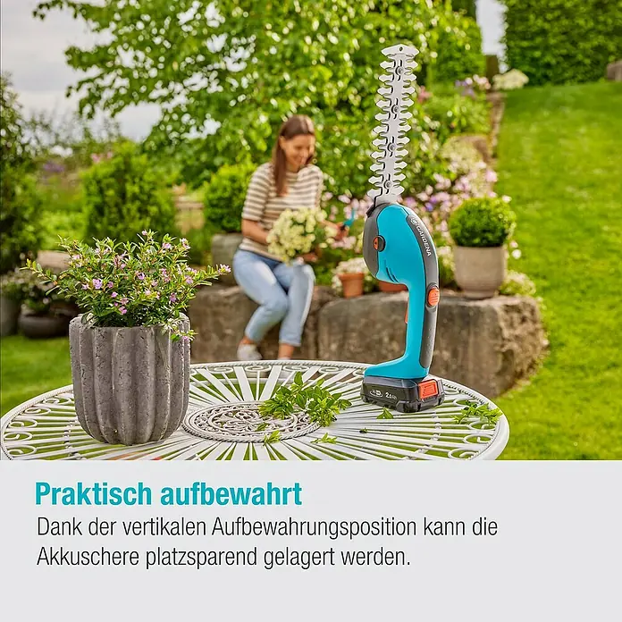 Gardena Power for All 18V Akku-Gras- & Strauchschere 20/18V P4A - 18 V, Li-Ionen, Ohne Akku - Die Gardena Akku-Grasschere steht auf einem Tisch im Garten. Dank der vertikalen Position ist die Lagerung platzsparend.