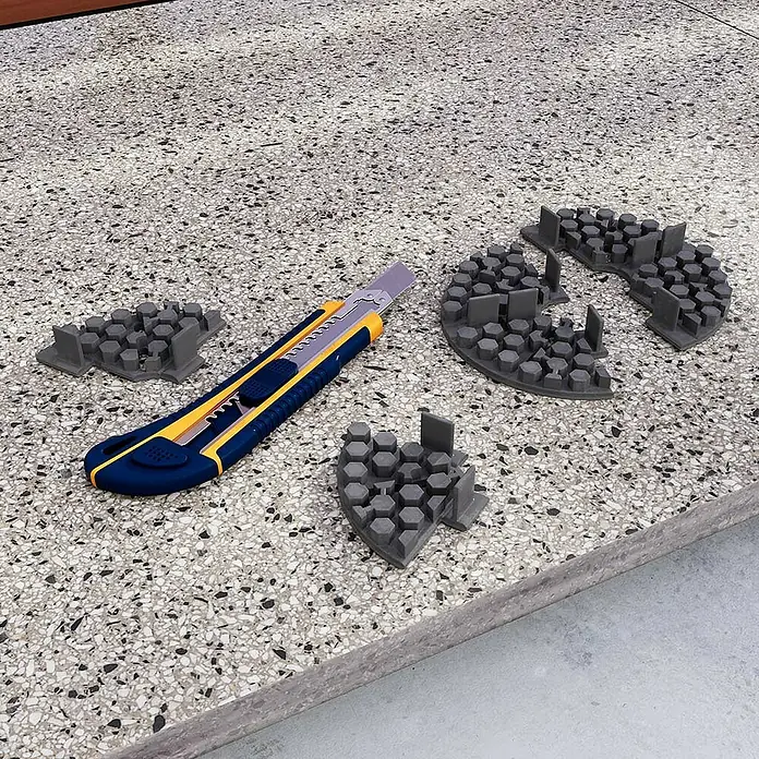 Langfit Plattenlager - 10 Stk., Kunststoff, Fugenbreite 3 mm - Nahaufnahme von Werkzeugen und 3D-gedruckten Objekten auf einer gesprenkelten Oberfläche.