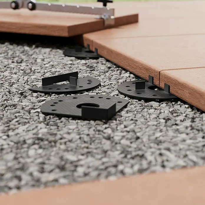 Langfit Kieslager - 10 Stk., Kunststoff, Ganze Scheibe - Detailaufnahme von Terrassenplatten, die mit schwarzen Abstandshaltern auf Kies verlegt werden. Ein Werkzeug liegt oben auf.