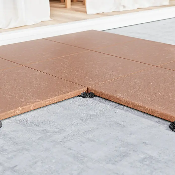 Langfit Plattenlager - 10 Stk., Kunststoff, Fugenbreite 3 mm - Braune Terrassenfliesen mit schwarzen Abstandshaltern auf einem grauen Untergrund. Das Produkt sorgt für eine moderne und ebene Fläche im Außenbereich.