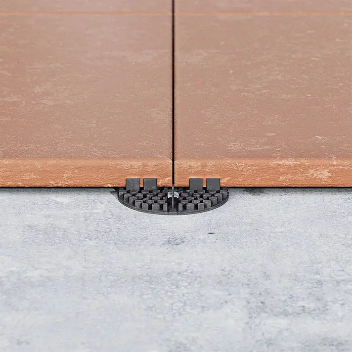 Langfit Plattenlager - 10 Stk., Kunststoff, Fugenbreite 3 mm - Nahaufnahme eines Terrassenplattenabstandshalters zwischen zwei braunen Fliesen auf grauem Untergrund.