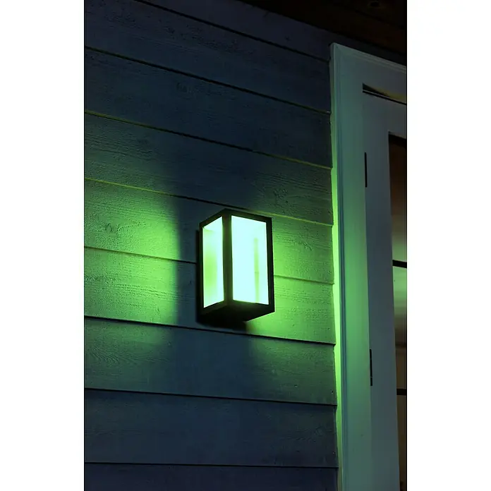 Philips Hue LED-Außenwandleuchte Impress - 8 W, 14,1 x 12 x 24 cm, Schwarz, IP44 - Nahaufnahme einer modernen Außenwandleuchte, die ein helles, grünes Licht ausstrahlt und an einer Wand mit Holzverkleidung befestigt ist.