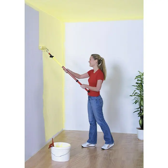 Lehnartz Farbroller Paint-Stick XXL - Breite Rolle: 230 mm, Längenverstellung: 950 mm - 1.500 mm - Frau streicht eine Wand mit einem Farbroller und Teleskopstiel gelb. Malerarbeiten leicht gemacht mit dem richtigen Werkzeug.