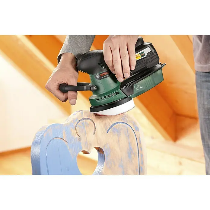 Bosch Power for All 18V Maschinenpaket - Akku-Exzenterschleifer AdvancedOrbit 18 + gratis Starter-Kit - Ein Akku-Exzenterschleifer von Bosch wird zum Abschleifen eines Holzstuhls mit Herzdesign verwendet, ideal für Renovierungsarbeiten.
