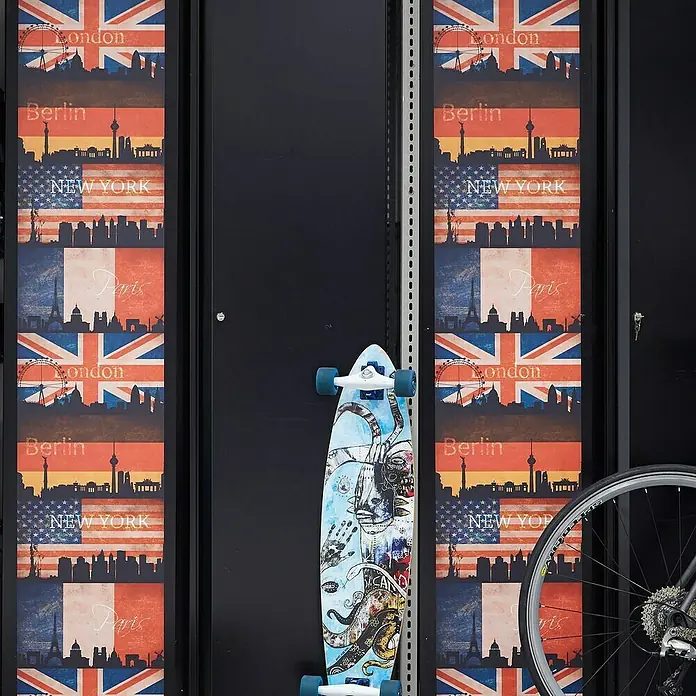 A.S. Création Designpanel pop.up - Städte, Bunt, 35 cm x 2,5 m - Skateboard mit blauem Oktopus-Design, lehnt an einer schwarzen Wand mit Stadtmotiven und einem Fahrrad im Hintergrund.
