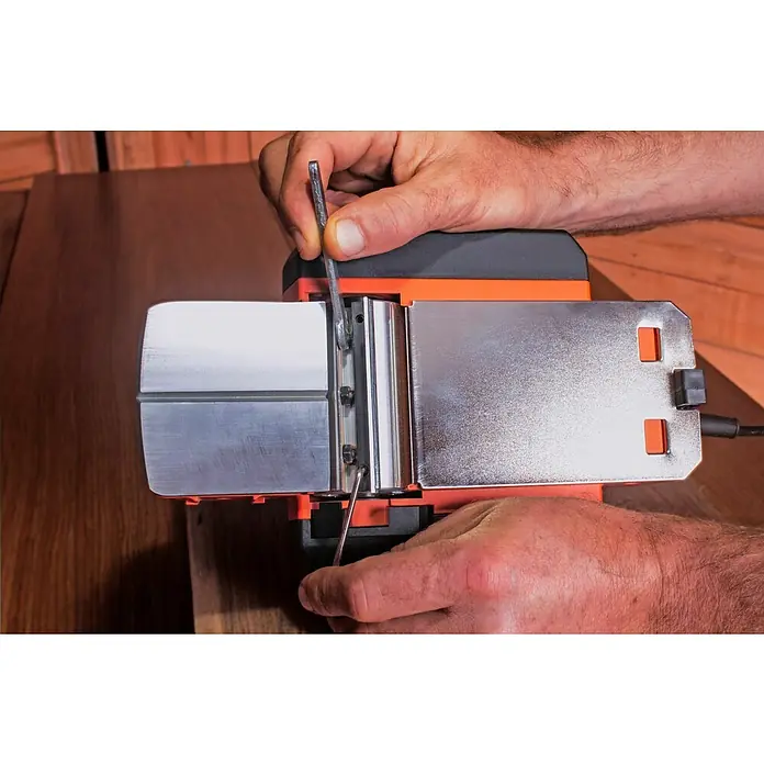 Black+Decker Cepilladora eléctrica BEW712 - 710 W, Profundidad de cepillo: 2 mm, Número de revoluciones de marcha en vacío: 16.500 r.p.m. - Un hombre ajusta una cepilladora eléctrica con una llave Allen, asegurando la precisión para el trabajo de la madera. La herramienta es esencial.