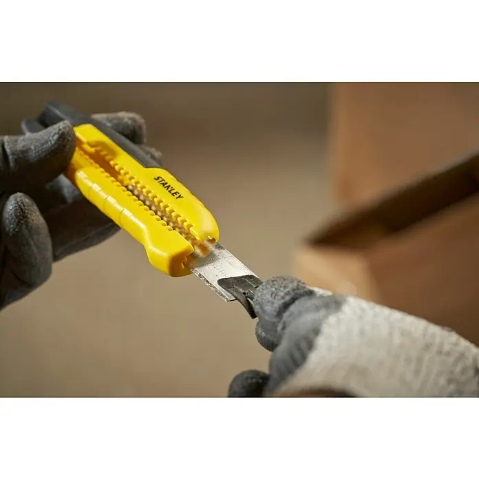 Stanley Cuchillo cúter STHT10489-0 - Plástico, Amarillo/Negro - Un cúter Stanley amarillo y negro sujeto por dos manos enguantadas que sirve para cortar una caja de cartón.