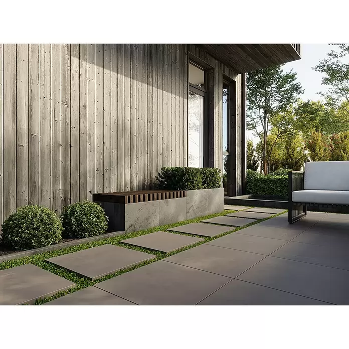 Terrassenfliese Modena - 80 x 80 x 2 cm, Ash/Graubraun, Matt - Moderner Außenbereich mit dunkelgrauen Pflastersteinen, Betonelementen und dunkler Holzwand, umgeben von Grünpflanzen.