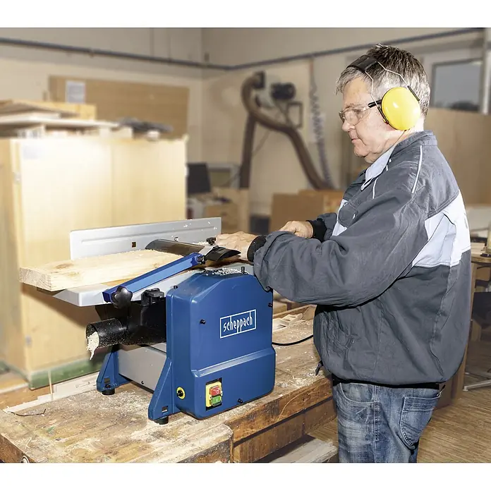 Scheppach Máquina de cepillado HMS 850 - 1.250 W - Un hombre utiliza una cepilladora Scheppach en un taller para trabajar la madera, llevando protectores auditivos amarillos.