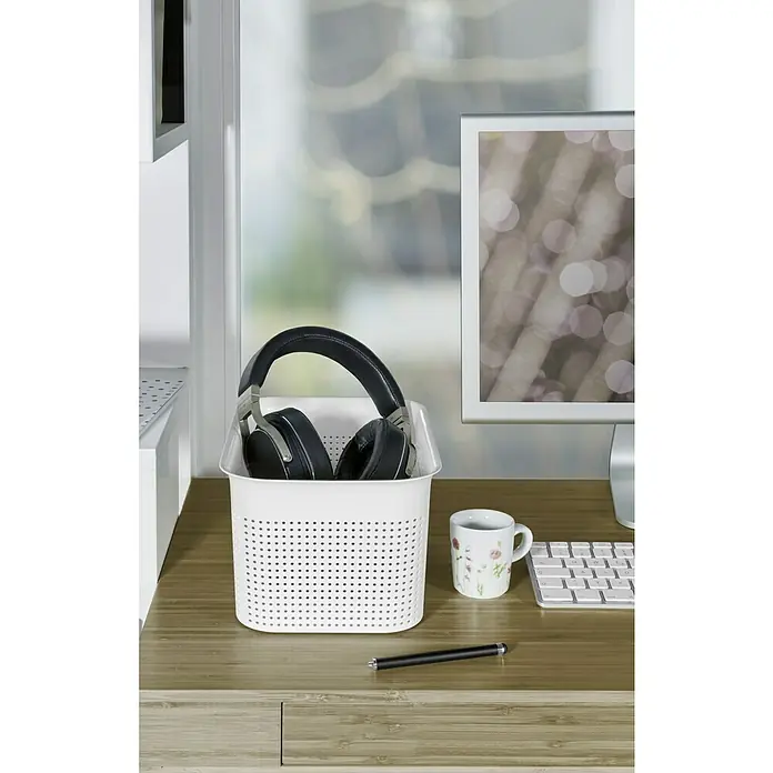 Rotho Aufbewahrungsbox Brisen - L x B x H: 26,2 x 18 x 13 cm, Kunststoff, Weiß - Kopfhörer in einem perforierten weißen Korb auf einem Schreibtisch mit Tasse, Stift, Tastatur und Monitor.