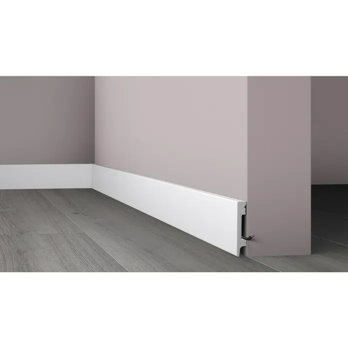 Nmc Decoflair Moldura de poliestireno decorativa M80 - 2 m x 1,3 cm x 5,8 cm, Polímero extruido de alta densidad (HDPS) - Primer plano de un zócalo blanco contra una pared, creando una transición elegante al piso de madera gris.
