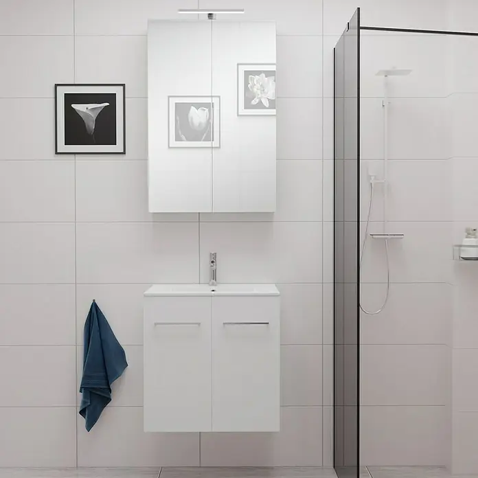 Camargue Espacio Badmöbel-Set E61 - 60 cm, Mira - Ein Badezimmer mit weißem Waschtisch, Spiegelschrank und Dusche. Die Fliesen sind ebenfalls weiß und es hängt ein blaues Handtuch.