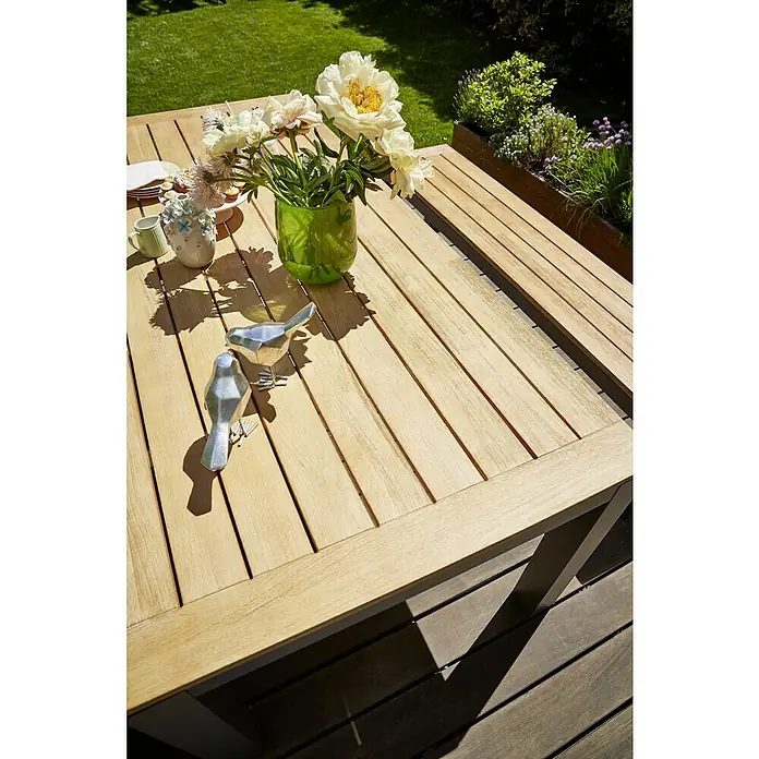 Sunfun Gartentisch Lynn - L x B x H: 220 x 100 x 76 cm, Akazie, Aluminium, Teakbraun, Anthrazit - Nahaufnahme eines Gartentisches mit Dekorationen, darunter Blumen in einer Vase und zwei silberne Vögel.