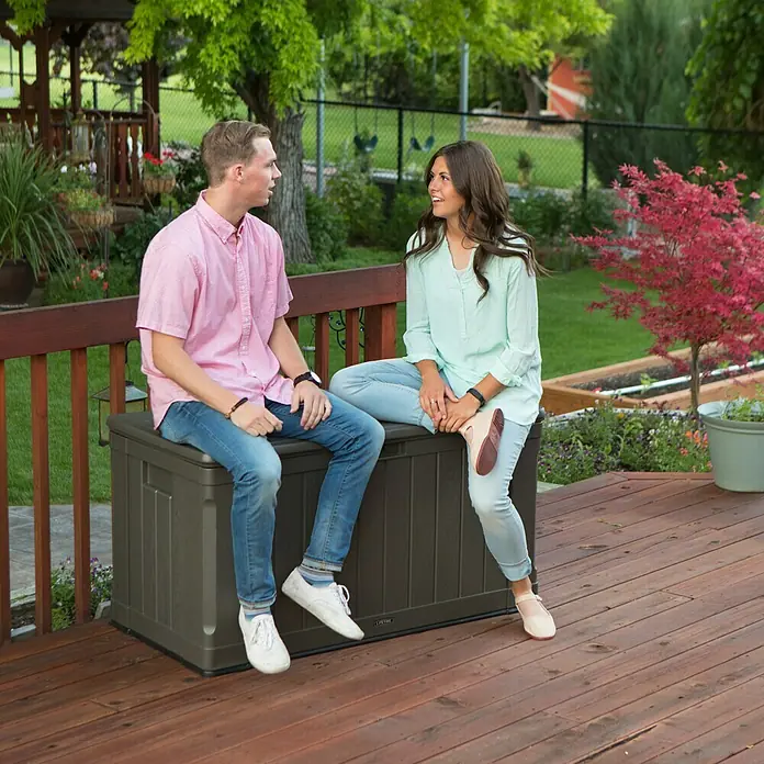 Lifetime Auflagenbox Harmony - 128 x 64 x 67 cm, Kunststoff, Braun - Zwei Personen sitzen auf einer Lifetime Aufbewahrungsbox im Freien. Die robuste Box bietet viel Stauraum und dient gleichzeitig als Sitzgelegenheit.