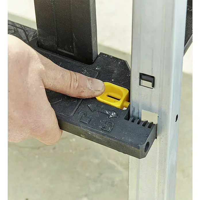 Stanley FatMax Werkzeugkasten FMST81083-1 - L x B x H: 29,6 x 64 x 28,7 cm, Klappbar - Nahaufnahme einer Person, die an einer klappbaren Arbeitsplattform eine gelbe Verriegelung betätigt, um die Höhe zu verstellen.