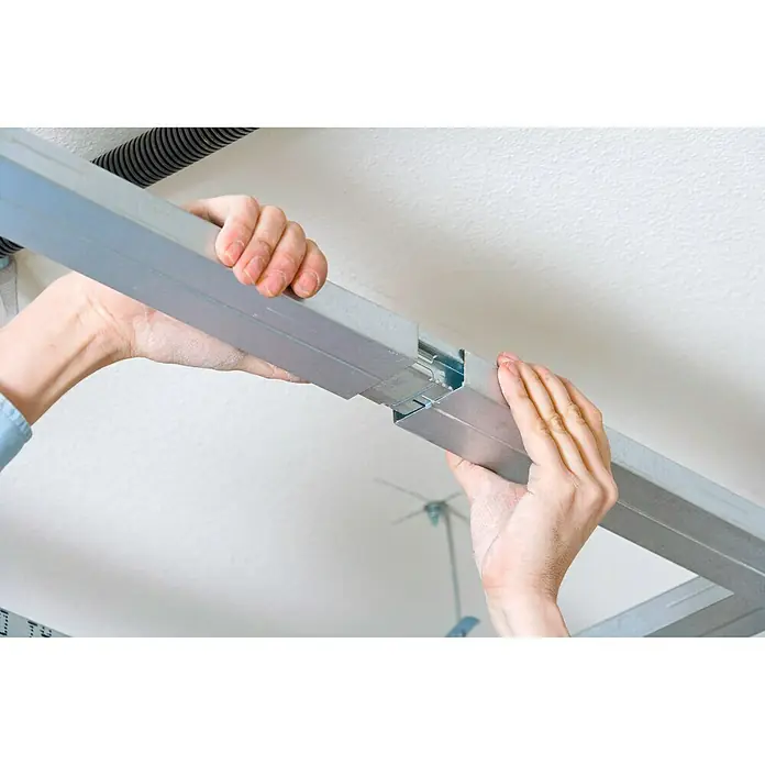 Knauf CD-Multiverbinder - 1 Stk. - Eine Person verbindet zwei silberne Metallschienen für eine abgehängte Deckenkonstruktion. Die Hände sind im Detail zu sehen.