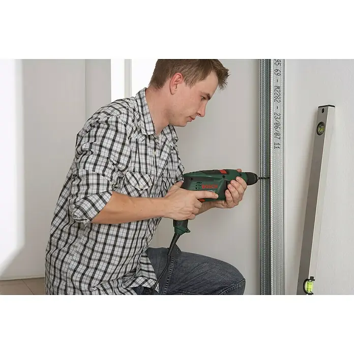 Knauf CW-Standprofil - 3.500 x 50 x 50 mm, Stahl - Ein Mann kniet und benutzt einen grünen Bosch-Bohrer, um in einen Metallständer zu bohren, während eine Wasserwaage daneben steht.
