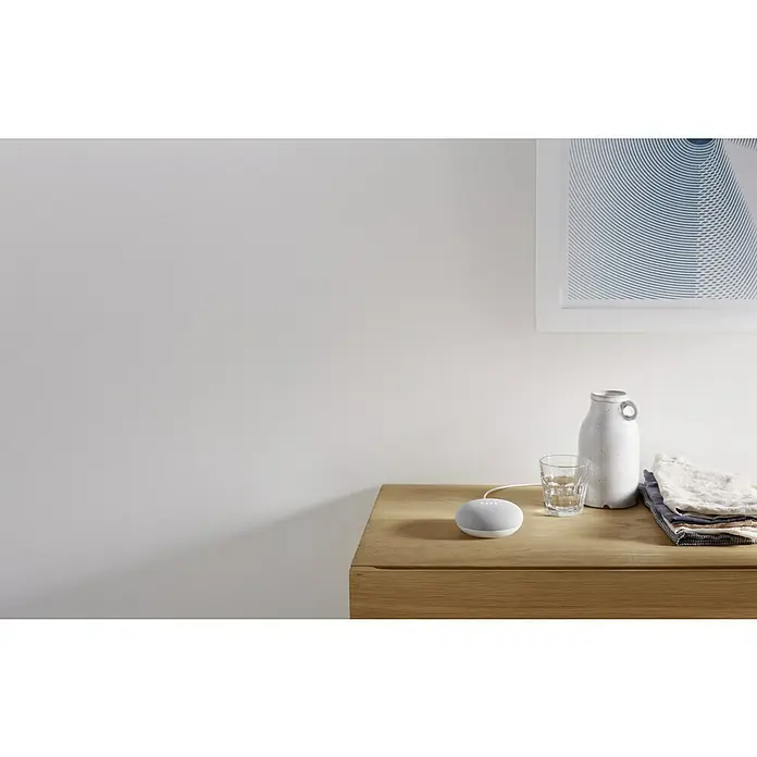 Google Nest Starter-Set Ledvance Smart+ BT Leuchtmittel - Kreide, 5,5 W, E27, Warmweiß, Dimmbar - Ein Google Nest Mini Smart-Lautsprecher auf einem Nachttisch neben einem Glas Wasser, einer Vase und Textilien.