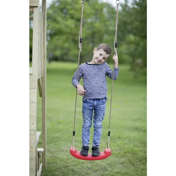 Wendi Toys Kinderspielturm Pelikan - Natur/Gelb - Ein fröhlicher Junge schaukelt auf einer roten Schaukel mit Seilen. Er steht auf der Schaukel und hält sich an den Seilen fest.