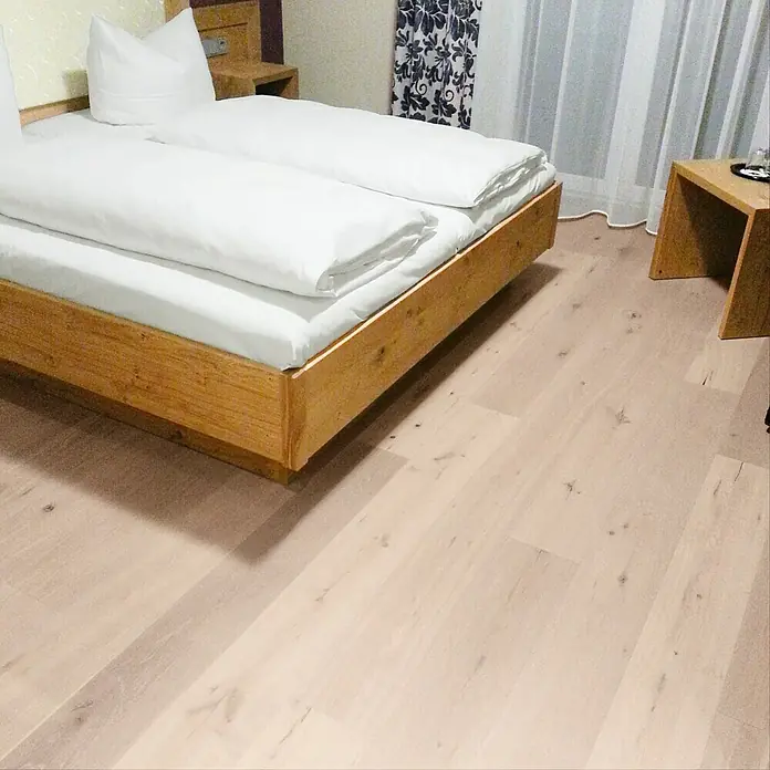 Fertigparkett Eiche Zürich1.250 x 190 x 14 mm, Landhausdiele - Nahaufnahme eines Bettes mit weißer Bettwäsche und Holzbettgestell, das eine komfortable und entspannende Atmosphäre bietet.