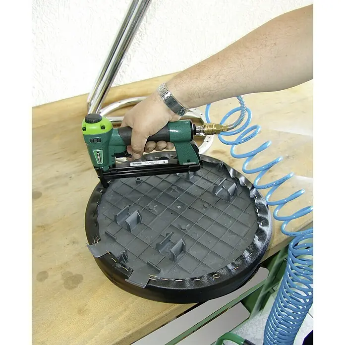 Prebena Druckluftnagler 1XR-A16 - Betriebsdruck: 4 bar - 7 bar, Passend für: Prebena Heftklammern der Type A von 4 - 16 mm - Befestigen eines schwarzen Stuhlsitzes mit einem grünen Tacker und einem blauen Luftschlauch. Handwerker bei der Arbeit an Möbeln in der Werkstatt.