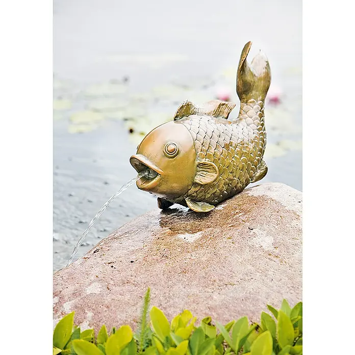 Heissner Wasserspeier Big Fish - Fisch, ½″ - Bronze Fisch-Gartenbrunnen auf einem Stein, Wasserstrahl aus dem Maul, umgeben von grüner Bepflanzung und Wasser.
