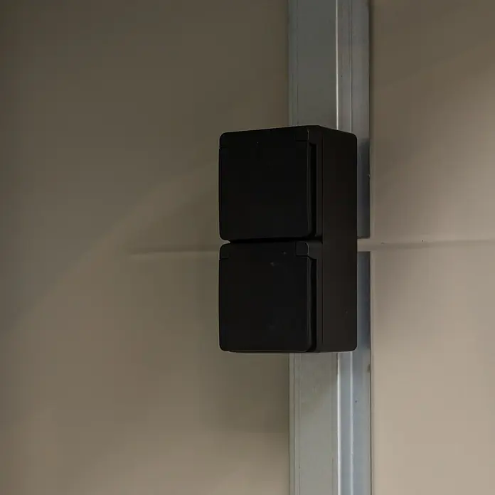 Telluria Fahrradgarage - Stahl, Anthrazit - Ein schwarzer, doppelter Stromanschluss ist an einer Metallschiene an einer hellen Wand montiert. Praktische Lösung für Strombedarf.