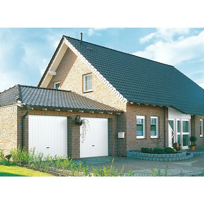 Novoferm Puerta de garaje Perfect - 2,5 x 2,15 m, Blanco - Vista de una casa residencial con dos puertas de garaje blancas. El edificio de ladrillo tiene un techo de tejas oscuras y zonas verdes bien cuidadas.