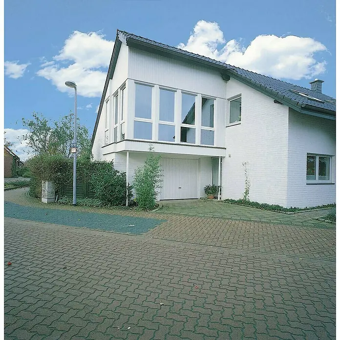 Novoferm Puerta de garaje Perfect - 2,5 x 2,15 m, Blanco - Casa moderna y luminosa con garaje y grandes ventanales bajo un cielo azul, rodeada de un camino pavimentado y vegetación exuberante.