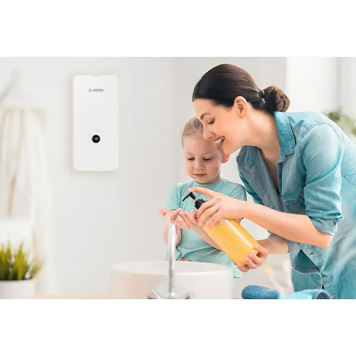 Bosch Durchlauferhitzer Tronic Advanced AquaStop - 21/24/27 kW, Elektronisch - Eine Mutter mit Tochter, die sich die Hände mit Seife wäscht, und einem Bosch Warmwasserbereiter an der Wand.