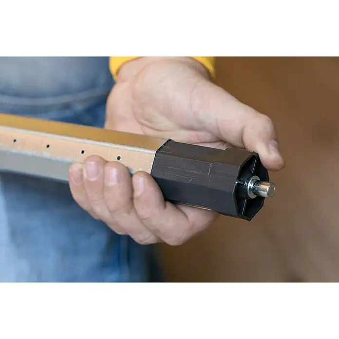 Schellenberg Funk-Rohrmotor Premium 6 MiniMax. Rollladenfläche: 4 m² bei Kunststoffrollläden, Einbaulänge: 570 mm, Zugkraft: 15 kg - Nahaufnahme eines Aluminiumrollladenprofils mit schwarzer Endkappe und Metallstift, das in einer Hand gehalten wird.