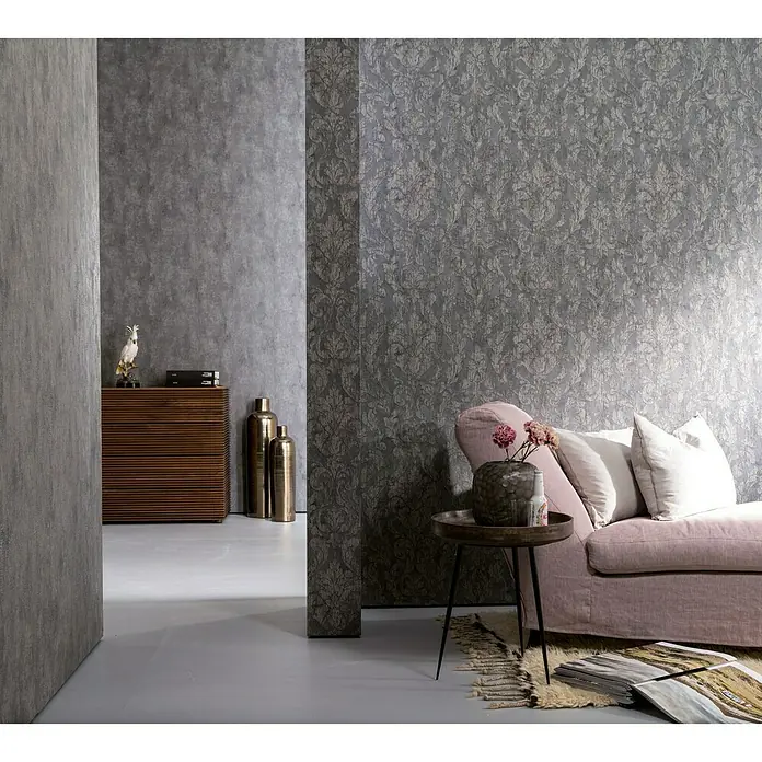 Marburg Nabucco Vliestapete Shadow - Dunkelgrau, Uni, 10,05 x 0,53 m - Nahaufnahme eines eleganten Wohnzimmers mit einer grauen gemusterten Tapete, einem rosa Sofa und einem Beistelltisch mit Blumen.