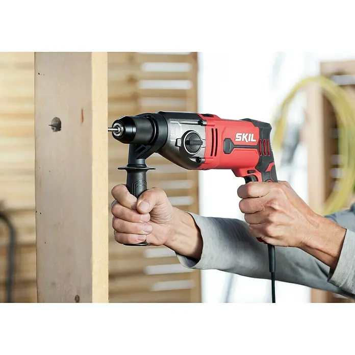 Skil Schlagbohrmaschine 6745 GA - 1.050 W, Schnellspannbohrfutter - Ein roter Skil-Bohrer wird verwendet, um ein Loch in ein Stück Holz zu bohren. Ideal für Heimwerkerprojekte und professionelle Anwendungen.
