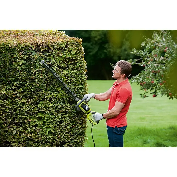 Ryobi Cortasetos eléctrico RHT6160RL - 600 W, Longitud de corte: 60 cm - Un hombre corta un seto con un cortasetos Ryobi para mantener y dar forma a su jardín.