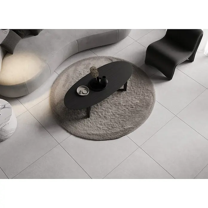 Feinsteinzeugfliese Giant - 79,7 x 79,7 cm, Weiß, Matt - Ein elegantes Wohnzimmer mit einem ovalen Couchtisch auf einem runden Teppich, ergänzt durch ein graues Sofa und einen stilvollen Sessel.