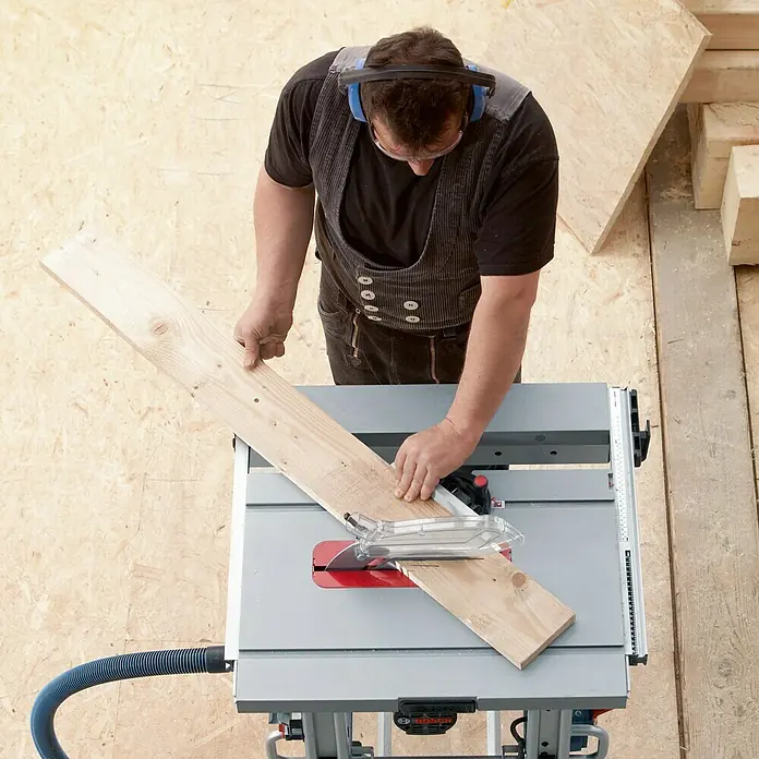 Bosch Professional Tischkreissäge GTS 10 J - 1.800 W, Durchmesser Sägeblatt: 254 mm, Schnitttiefe bei 90 °: 79 mm - Ein Handwerker arbeitet mit einer Bosch Tischkreissäge, um ein Holzbrett präzise zuzuschneiden. Die Säge steht sicher auf einem Arbeitstisch.