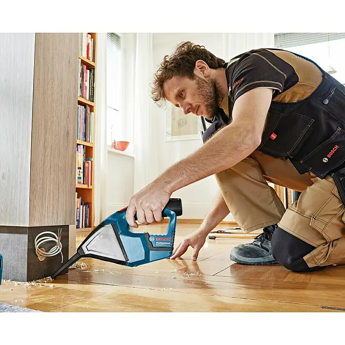 Bosch Professional Akku-Handstaubsauger GAS 12V - 12 V, Li-Ionen, Ohne Akku, Luftmenge: 15 l/s, Karton - Ein Mann benutzt einen Bosch Professional Staubsauger, um Sägespäne vom Boden zu entfernen. Der blaue Staubsauger ist gut sichtbar.