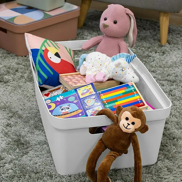 Sunware Aufbewahrungsbox Sigma Home - L x B x H: 59 x 39 x 24,2 cm, Kunststoff, Weiß - Ein weißer Spielzeugkorb gefüllt mit verschiedenen Spielsachen, darunter ein Plüschhase, ein Einhorn und ein Stoffaffe, steht auf einem grauen Teppich.