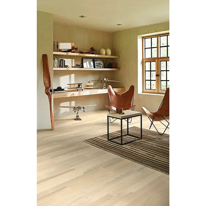 Parador Parkettmuster Classic 3060 Living Esche - 200 x 185 x 13 mm, Schiffsboden - Einladender Raum mit hellem Holzboden, Modellflugzeugen und zwei Ledersesseln, die eine warme und stilvolle Atmosphäre schaffen.