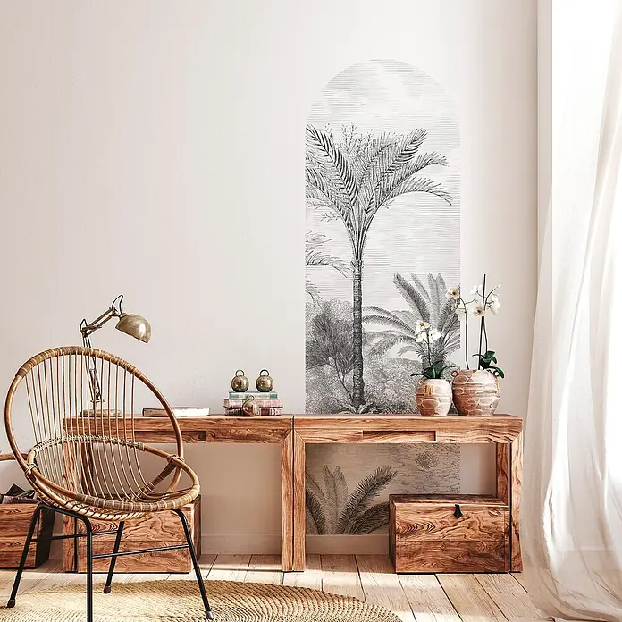 Vinilo de pared autoadhesivo Arco Old Jungle - 65 x 200 cm, Blanco/Negro, Plástico - Rincón de lectura acogedor con una silla de ratán sobre una alfombra tejida, un escritorio de madera y arte de pared de temática tropical.