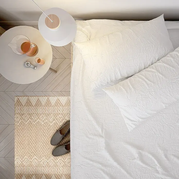 Alfombra de vinilo Telma - Natural, 75 x 48 cm, PVC - Atractivo bodegón de dormitorio con una elegante cama con sábanas blancas, una lámpara, una mesita y zapatillas en la alfombra.
