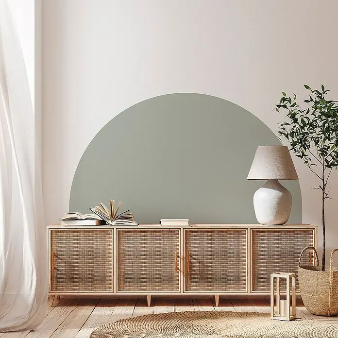 Vinilo de pared autoadhesivo Arco Verde Eucalipto - 132 x 170 cm, Verde, Plástico - La imagen muestra un elegante aparador con puertas de ratán tejido, decorado con libros y una lámpara, que irradia elegancia moderna en un entorno ligero y aireado.