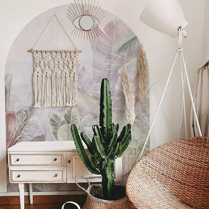 Vinilo de pared autoadhesivo Arco Tropic Sage - 132 x 170 cm, Multicolor, Plástico - Interior elegante con un cactus en una cesta, un tapiz de macramé y un espejo en forma de sol sobre un papel pintado botánico.